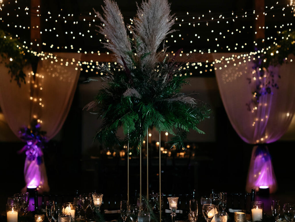 tall greenery arrangement on table with lights and drapes in background